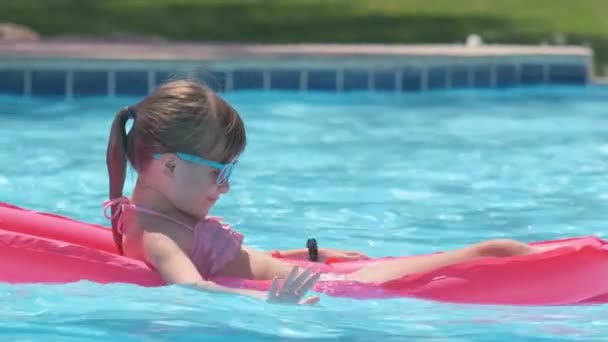 Young joyful child girl having fun swimming on inflatable air mattress in swimming pool with blue water on warm summer day on tropical vacations. Summertime activities concept — Stock Video