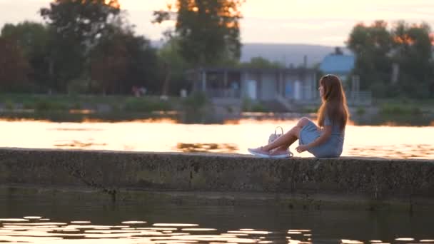 Jonge vrouw in casual outfit ontspannen aan meer kant op warme avond. Zomervakantie en reisconcept — Stockvideo