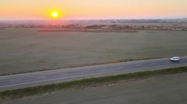 Gün batımında şehirlerarası yolda hızla giden yolcu aracının hava görüntüsü. Akşamları otoyol trafiği
