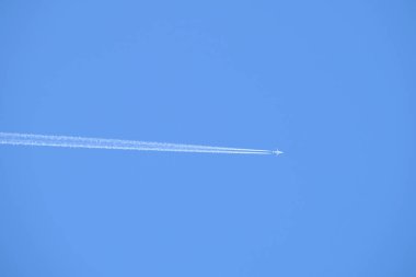Mesafeli yolcu jet uçağı açık mavi gökyüzünde yüksek irtifada uçarken ardında beyaz duman izi bırakıyor. Hava taşımacılığı kavramı
