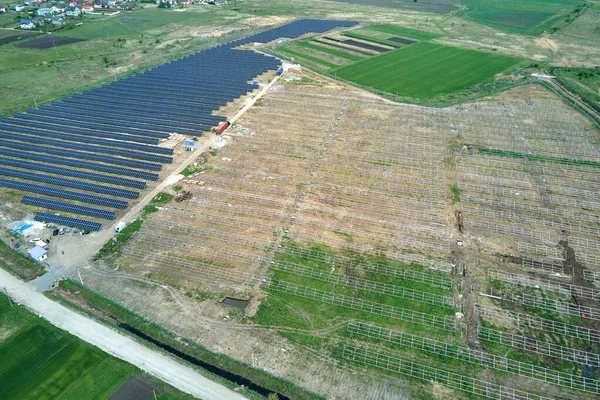Vista aérea de la gran planta de energía eléctrica en construcción con muchas filas de paneles solares en el marco de metal para producir energía eléctrica limpia. Desarrollo de fuentes de electricidad renovables — Foto de Stock