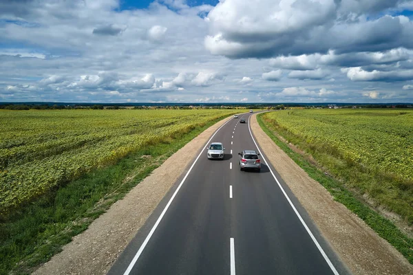 Вид с воздуха на междугороднюю дорогу между зелеными сельскохозяйственными полями с быстрыми автомобилями. Вид сверху с дрона дорожного движения — стоковое фото