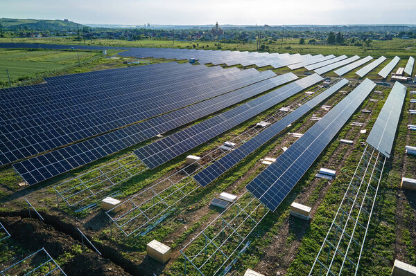 Aerial view of big electric power plant under construction with many rows of solar panels on metal frame for producing clean electrical energy. Development of renewable electricity sources