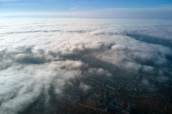 Aerial view from high altitude of distant city covered with puffy cumulus clouds flying by before rainstorm. Airplane point of view of landscape in cloudy weather — Stock Photo, Image