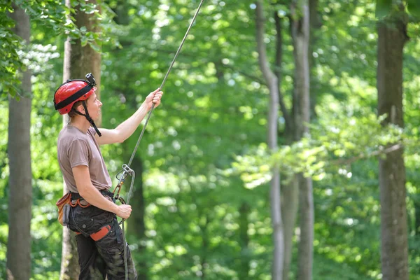 Adam bağlanma cihazı ve iple ortağını bağlıyor. Tırmanışçılar kaya dağcılığı güvenliği için ekipman tutuyor.