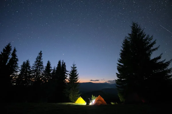 Tentes touristiques lumineuses éclairées près de feu de joie sur le camping dans les montagnes sombres sous le ciel nocturne avec des étoiles scintillantes. Concept de mode de vie actif — Photo