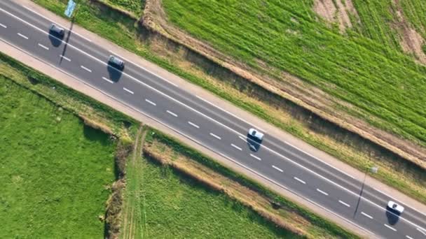 Luftaufnahme der Überlandstraße zwischen grünen landwirtschaftlichen Feldern mit schnell fahrenden Autos. Draufsicht von der Drohne auf den Autobahnverkehr — Stockvideo