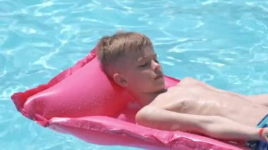 Genç çocuk tropik tatiller sırasında yüzme havuzunda şişme şişme yatakta yüzerek yaz güneşinde dinleniyor. Yaz etkinlikleri konsepti