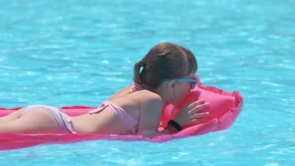 Niña alegre joven que se divierte nadando en el colchón inflable del aire en la piscina con el agua azul en el día caliente del verano en vacaciones tropicales. Concepto de actividades de verano — Vídeo de stock