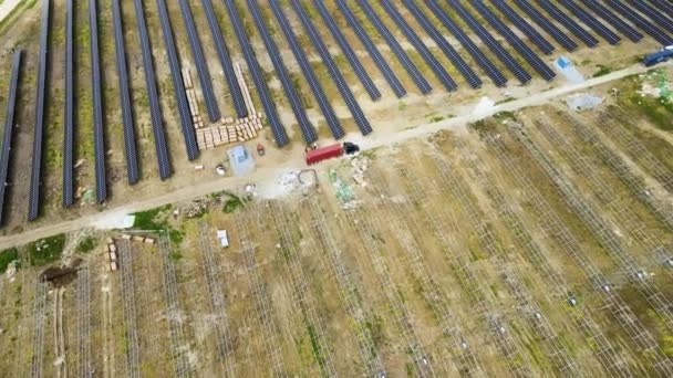 Vista aérea de la planta de energía eléctrica en construcción con camión entregando piezas de montaje para paneles solares en marco metálico para producir energía eléctrica. Desarrollo de la electricidad renovable — Vídeos de Stock