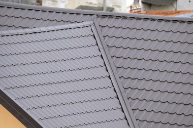 Evin çatısının üstü metalik kiremitlerle kaplı. Binanın üstü kartonla kaplı.