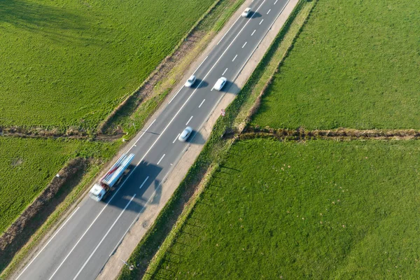 Luftaufnahme der Überlandstraße zwischen grünen landwirtschaftlichen Feldern mit schnell fahrenden Autos. Draufsicht von der Drohne auf den Autobahnverkehr — Stockfoto
