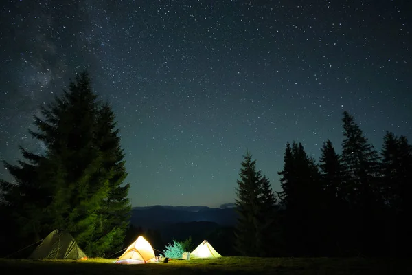 Parlak turist çadırları gece gökyüzünün altındaki karanlık dağlarda parlayan parlayan yıldızlarla. Etkin yaşam tarzı kavramı