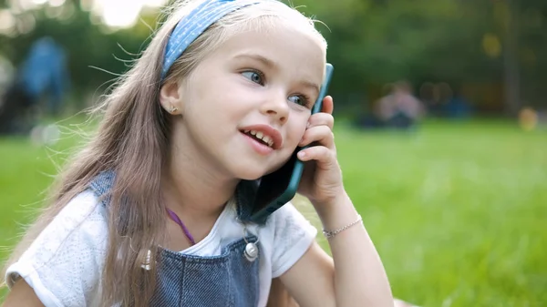 Happy little girl having conversation on mobile phone in summer park — Stok Foto