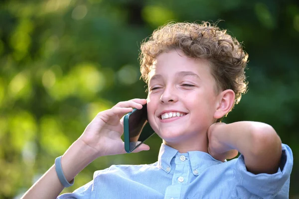 Счастливый мальчик разговаривает по сотовому на улице в летнем парке — стоковое фото
