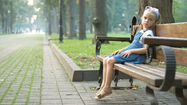 Küçük kız yaz parkında bankta tek başına oturuyor. — Stok fotoğraf