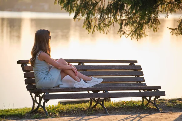 Samotna kobieta siedząca na ławce nad jeziorem ciesząca się ciepłym letnim wieczorem. Pojęcie samotności i relaksu — Zdjęcie stockowe