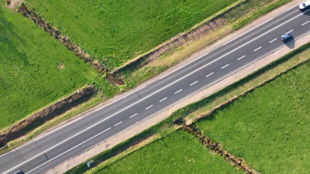 Luftaufnahme der Überlandstraße zwischen grünen landwirtschaftlichen Feldern mit schnell fahrenden Autos. Draufsicht von der Drohne auf den Autobahnverkehr — Stockvideo