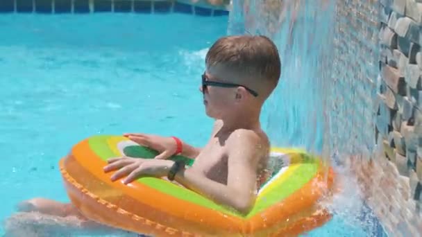 Genç neşeli çocuk tropikal tatillerde sıcak yaz gününde mavi suyla yüzme havuzunda şişme hava çemberinde yüzerken eğleniyor. Yaz etkinlikleri konsepti — Stok video