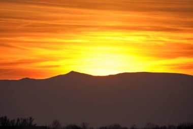 Güzel bir akşam panoramik manzarası. Gün batımında uzak dağ tepeleri üzerinde parlak batan güneş.