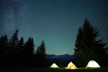 Gece yıldızlarının altındaki karanlık dağlardaki kamp alanında parlayan parlak kamp çadırları gökyüzünü kapladı. Aktif yaşam tarzı ve seyahat konsepti