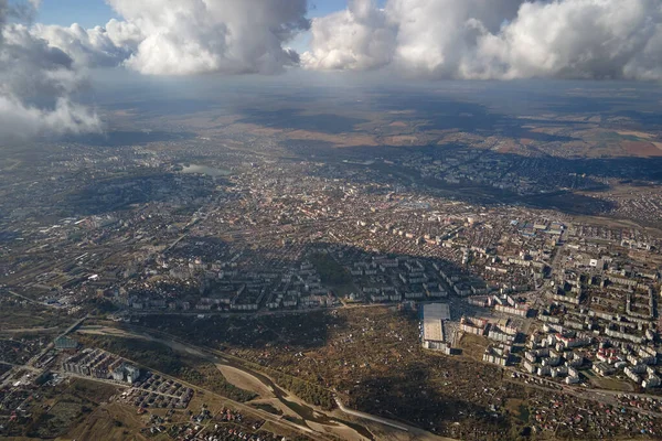 Luftaufnahme aus dem Flugzeugfenster in großer Höhe einer weit entfernten Stadt, die vor einem Regensturm mit geschwollenen Kumuluswolken bedeckt ist — Stockfoto