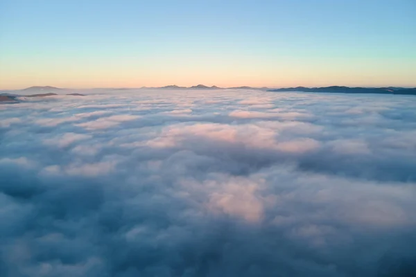 Aerial view of colorful sunrise over white dense fog with distant dark silhouettes of mountain hills on horizon — Stock Photo, Image