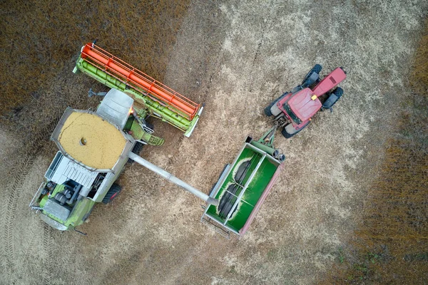 Vista aérea de la cosechadora que descarga el grano en el remolque de carga que trabaja durante la temporada de cosecha en un gran campo de trigo maduro. Agricultura y transporte del concepto de productos agrícolas crudos — Foto de Stock