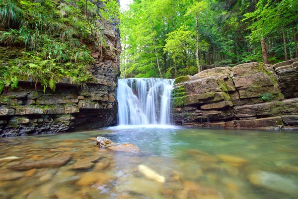 Yazın yağmur ormanlarında kayalık kayalıklardan dökülen beyaz köpüklü suyla dağ nehrindeki muhteşem şelale manzarası.