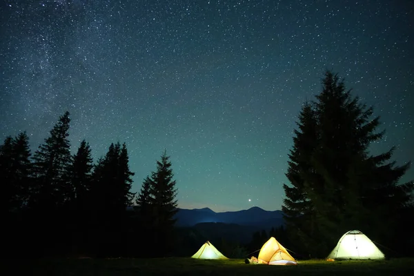 Ljusa belysta campingtält som lyser på campingplatsen i mörka berg under natts stjärnor täckt himmel. Aktiv livsstil och resande koncept — Stockfoto