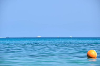 Mavi deniz suyunun dalgalı yüzeyi ve sakin dalgalar üzerinde yüzen uzak gemileri olan deniz burnu.