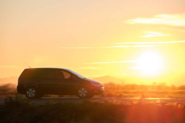 Gün batımında şehirlerarası yolda hızla giden bir SUV arabası. Akşamları otoyol trafiği