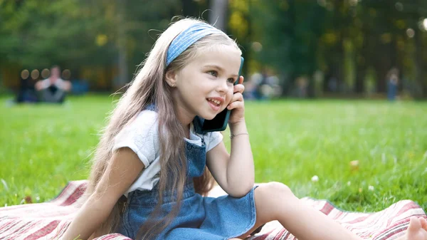 Bonne petite fille ayant conversation parler sur téléphone mobile dans le parc d'été — Photo