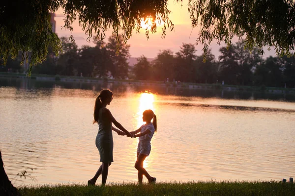 Happy mom and daughter girl relaxing holding hands enjoying time together in summer park at sunset. Family love and relationship concept — Stock Photo, Image