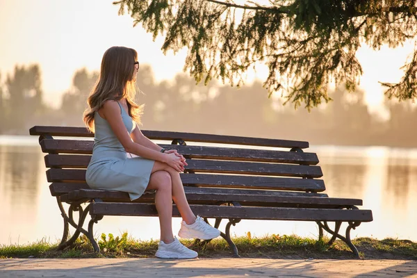 Einsame Frau, die an einem warmen Sommerabend allein auf der Bank am Seeufer sitzt. Einsamkeit und Entspannung in der Natur — Stockfoto