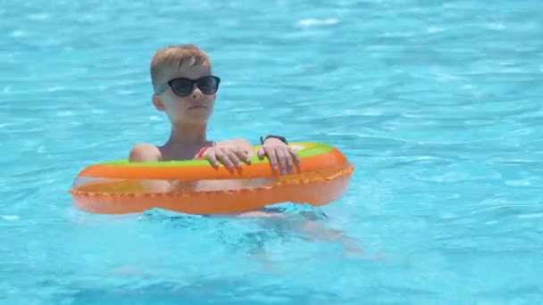 Niño alegre joven que se divierte nadando en círculo inflable del aire en la piscina con el agua azul en el día caliente del verano en vacaciones tropicales. Concepto de actividades de verano — Vídeo de stock