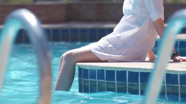Giovane ragazza gioiosa bambino a riposo sul lato della piscina con acqua limpida blu nella soleggiata giornata estiva. Concetto di vacanze tropicali — Video Stock