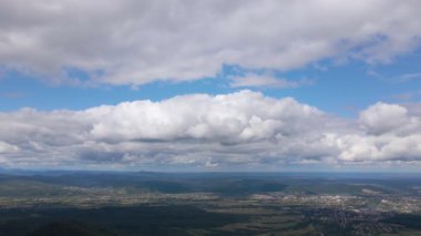 Fırtınadan önce, şişkin kümülüs bulutlarıyla kaplı uzak şehrin yüksek irtifasından gelen hava manzarası. Bulutlu havada uçak manzarası