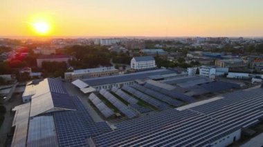 Akşamları yeşil ekolojik elektrik üretmek için endüstriyel binaların çatısına mavi fotovoltaik paneller monte edilmiş güneş enerjisi santralinin hava görüntüsü. Sürdürülebilir enerji konsepti üretimi