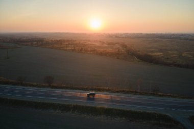 Gün batımında hızlı giden bulanık arabalı şehirlerarası yol manzarası. Akşamları otoban trafiğinin insansız hava aracı görüntüsü