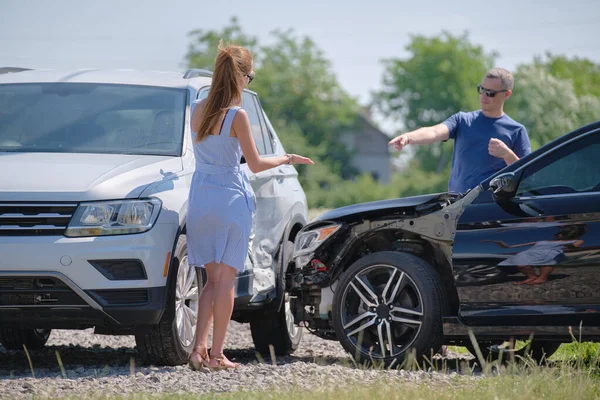 Angry woman and man drivers of heavily damaged vehicles arguing who is guilty in car crash accident on street side. Road safety and insurance concept