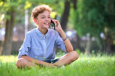 Yazlık parkta cep telefonuyla konuşan mutlu genç çocuk.