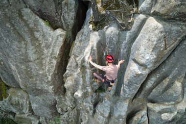 Genç adam dik kayalık dağ duvarına tırmanıyor. Erkek tırmanışçı zorlu rotayı aşar. Ekstrem spor konseptine dalmak