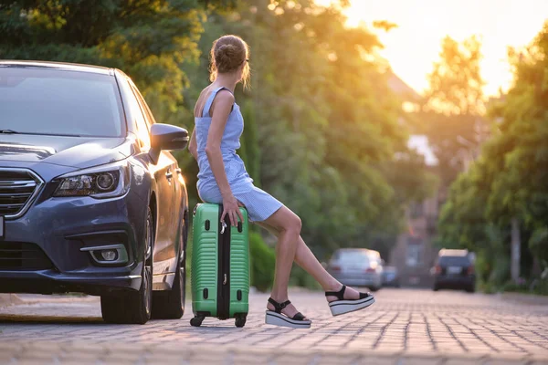 Junge müde Frau mit Koffer, die neben ihrem Auto sitzt und auf jemanden wartet. Reise- und Urlaubskonzept — Stockfoto