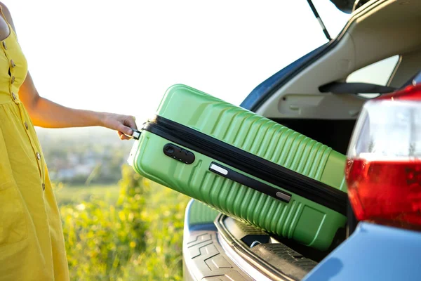 Großaufnahme von weiblichen Händen, die grüne Koffer aus dem Kofferraum holen. Reise- und Urlaubskonzept — Stockfoto