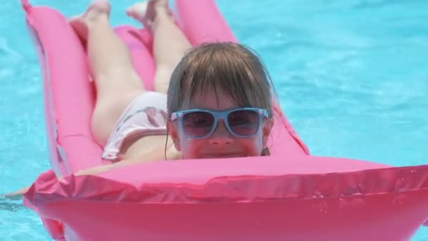 Happy child girl relaxing on inflatable air mattress in swimming pool on sunny summer day during tropical vacations. Summertime activities concept — Stock Video