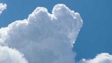 Beyaz kabarık kümülüs bulutlarının zamanı yaz mavi gökyüzünde şekilleniyor. Hareket eden ve değişen bulutlu hava durumu