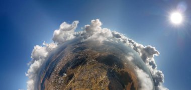 Aerial view from high altitude of little planet with distant city covered with puffy cumulus clouds flying by before rainstorm. Airplane point of view of landscape in cloudy weather