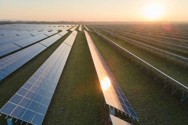 Günbatımında temiz elektrik enerjisi üretmek için birçok sıra güneş fotovoltaik paneli bulunan sürdürülebilir büyük elektrik santralinin havadan görünüşü. Sıfır emisyon kavramı ile yenilenebilir elektrik