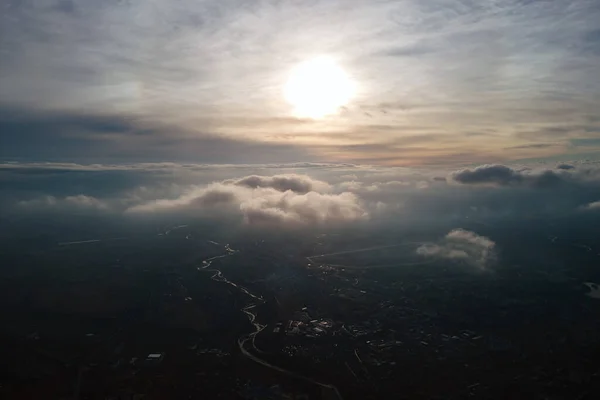Vista aérea desde la gran altitud de la ciudad distante cubierta de nubes de cúmulos hinchados que pasan volando antes de la tormenta al atardecer. Avión punto de vista del paisaje en tiempo nublado — Foto de Stock
